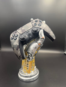 Gray Camouflage PS5 DualSense unit PS5-CMO-002 displayed on a silver robotic hand controller stand